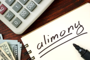 A calculator is on a desk with a handwritten note that spells out alimony.