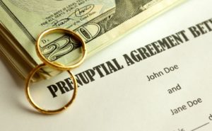 A twenty dollar bill, wedding rings, and a prenuptial agreement are shown in this photo. 